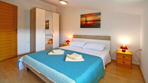 A neatly made bed with a blue quilt, two bedside tables with lamps, a wooden wardrobe, and a painting on the wall.