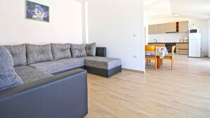 A modern living room with a sectional sofa, a dining table with chairs, and a kitchen area in the background.