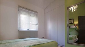 A bedroom with a bed, a window with blinds, a mirror, and a door.