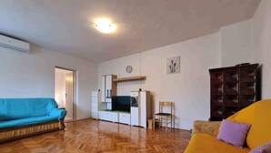 A living room with a herringbone wooden floor, a teal sofa, a yellow sofa with a purple pillow, a wooden cabinet, and a television. - Holiday flat with air conditioning (Valbandon)