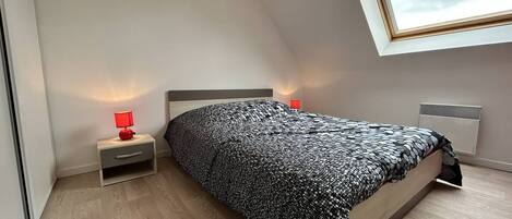 A bedroom with a bed, a nightstand, a red lamp, and a window with a view of the sky.