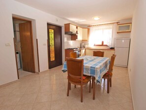 A compact kitchen with a dining area, featuring a tiled floor, wooden chairs, and a table with a blue and white tablecloth.