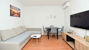 A modern living room with a sofa, dining table, chairs, a TV, and a painting on the wall. - Holiday apartment with air conditioning (Štinjan)
