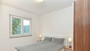 A bedroom with a bed, two bedside tables with lamps, a window, and a wooden door. - Holiday apartment with air conditioning (Štinjan)