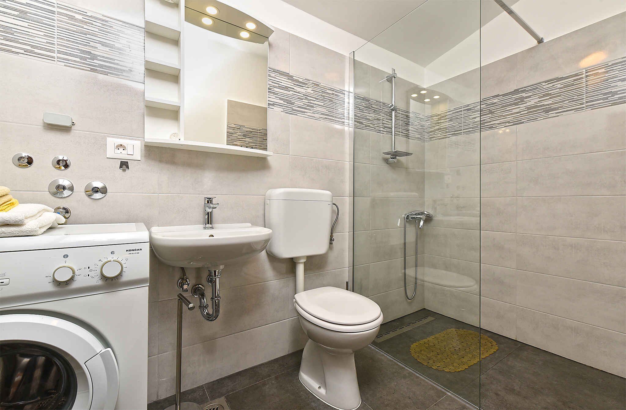 A modern bathroom with a washing machine, a sink, a toilet, and a glass shower enclosure.