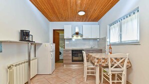 Une cuisine de taille réduite avec un plafond en bois, une table à manger recouverte d’une nappe à motifs et un réfrigérateur blanc.