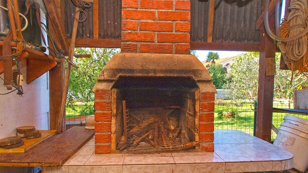 A brick-built wood-fired oven with a stone base, surrounded by rustic wooden beams and a metal fence. - Holiday apartment with air conditioning (Valbandon)