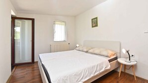 Un dormitori amb un llit, una taula de nit amb una làmpada, una finestra amb cortines i un radiador.