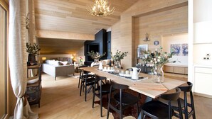 A spacious living area with a wooden ceiling, a dining table set with chairs, and a cozy seating area with a sofa and cushions.