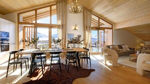 A spacious living room with a large wooden ceiling, a dining area with a table and chairs, and a view of mountains through large windows.