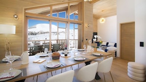 A dining area with a large table set for six, a view of a snowy landscape, and a modern interior with wooden beams and large windows.