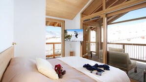 A bedroom with a large bed, a TV on the wall, and a view of a snowy landscape through a balcony.