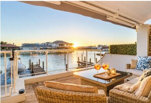 A balcony with wicker furniture, a glass table, and two glasses of drink. - Baruna Dock Canal View (Halls Head)