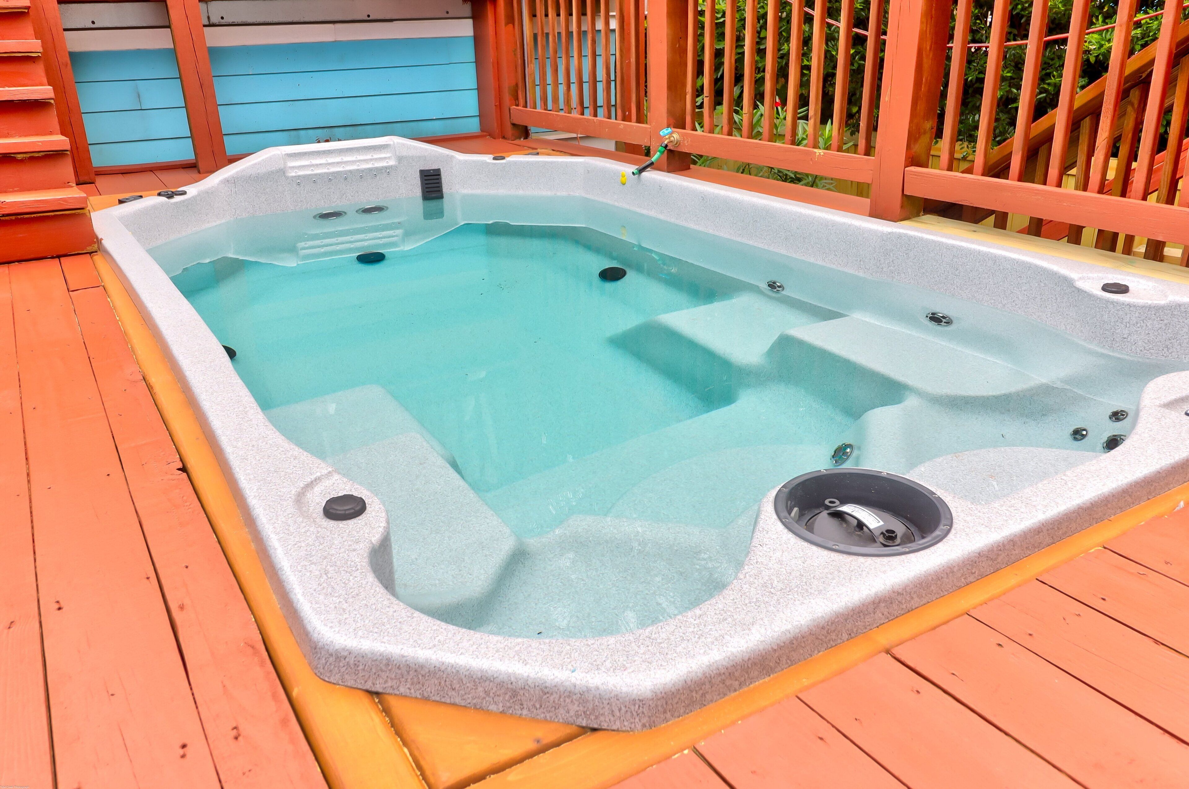 Ein Whirlpool auf einer Holzterrasse mit Metallgeländer und einer blauen Wand im Hintergrund.