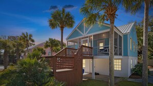 A two-story house with a porch, surrounded by palm trees and a wooden fence. - Swim Spa, Tiki Bar, Pet friendly, Fenced yard, 3 min walk to beach - The Blue House (Isle Of Palms)