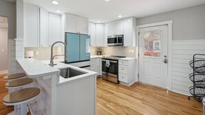 A modern kitchen with white cabinets, a blue refrigerator, stainless steel appliances, and wooden bar stools. - Swim Spa, Tiki Bar, Pet friendly, Fenced yard, 3 min walk to beach - The Blue House (Isle Of Palms)