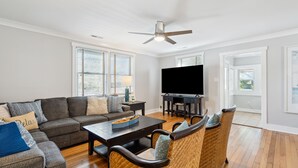 A living room with a sofa, chairs, a coffee table, a TV, and a ceiling fan. - Oasis w/ Private Pool, Pets considered, 2 Houses from beach access- The Pink House (Isle Of Palms)
