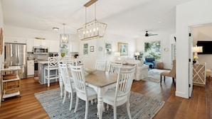 A spacious kitchen with white cabinetry, a stainless steel refrigerator, and a microwave. There is a dining area with a wooden table and white chairs. - 501 MOORINGS - Marina View, Pool. Fully renovated. Perfect for Family, Boaters, Golfers (Isle Of Palms)