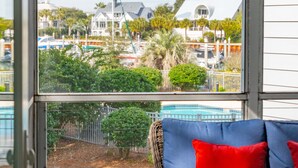 A room with a wicker sofa and a small round table, a view of a swimming pool, and a clear sky. - 501 MOORINGS - Marina View, Pool. Fully renovated. Perfect for Family, Boaters, Golfers (Isle Of Palms)