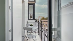 Un balcon avec une table et des chaises, un pot de fleurs et une vue sur la rue.