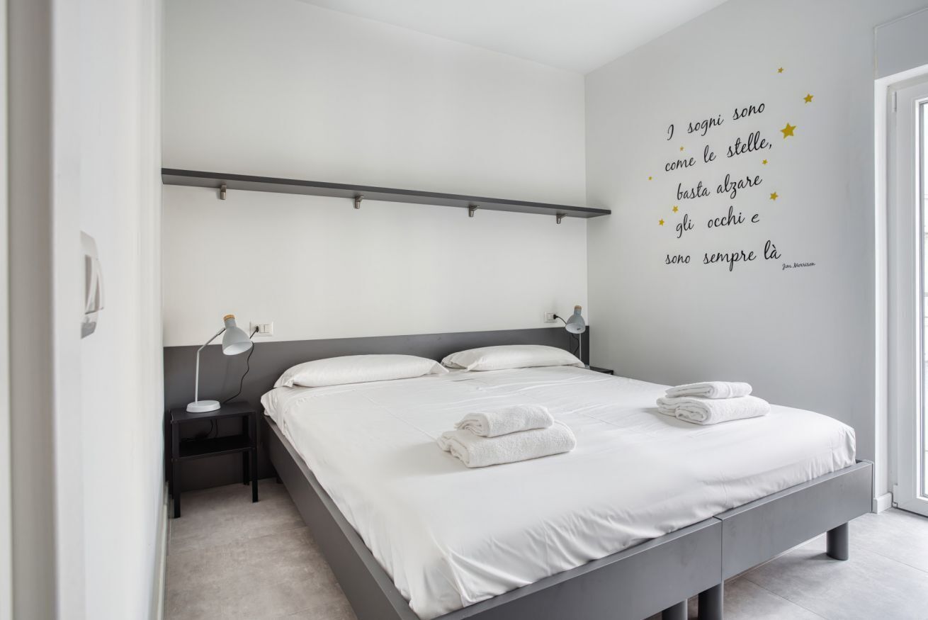 Une chambre à coucher comprenant un lit, des tables de chevet, une étagère fixée au mur et une citation inspirante.