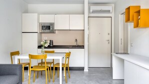 Une cuisine compacte avec des meubles blancs, un four à micro-ondes et un évier. On y trouve une table à manger avec des chaises et un canapé.