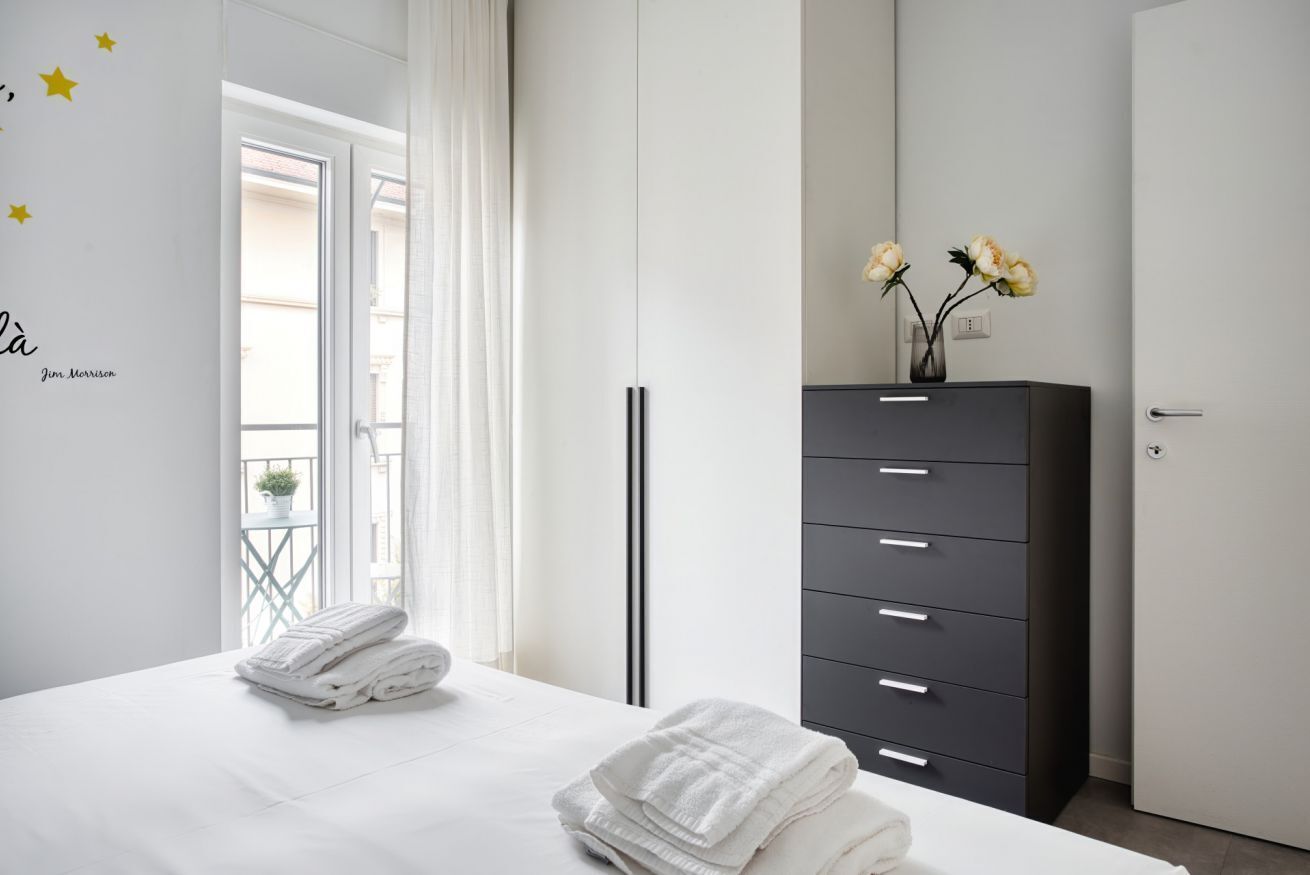 Un dormitorio con cama, cómoda, puerta y ventana con cortinas.