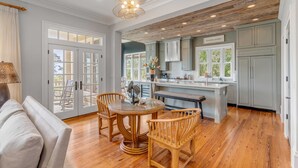 A spacious kitchen with wooden flooring, a dining area with a round table and chairs, and a view of the outdoors through large glass doors. - 7 Bedroom Oceanview Kiawah Vanderhorst Estate with Pool (Kiawah Island)