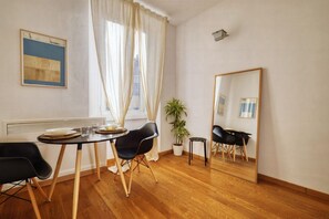 A room with a dining table, chairs, a potted plant, a mirror, and a radiator.
