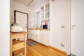 A compact kitchen with white cabinets, a microwave, a kettle, and a small window with glass doors.