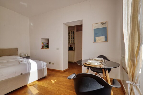 A hotel room with a bed, a dining table with chairs, a small kitchen area, and a framed picture on the wall.