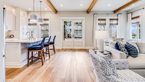 Une cuisine spacieuse avec un plancher en bois, un coin repas doté de tabourets de bar et un salon avec un canapé et des coussins.