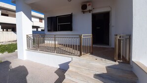Una entrada de edificio con baranda metálica, una puerta y una unidad de aire acondicionado en la pared.