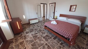 Un dormitorio con suelo de piedra, una cama con colcha a cuadros, una mesita de noche con lámpara y un armario.