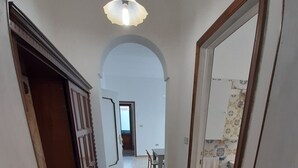 Un pasillo con suelo de piedra, un marco de puerta de madera y una lámpara colgante.