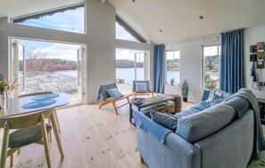 Un salón amplio con un sofá azul grande, dos sillones, una mesa de centro y vistas a un lago.