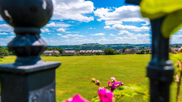A view of a green field with a distant hill and buildings.