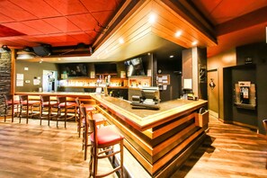 Una zona de bar con taburetes de madera, una barra con televisor y una pared de piedra de fondo.