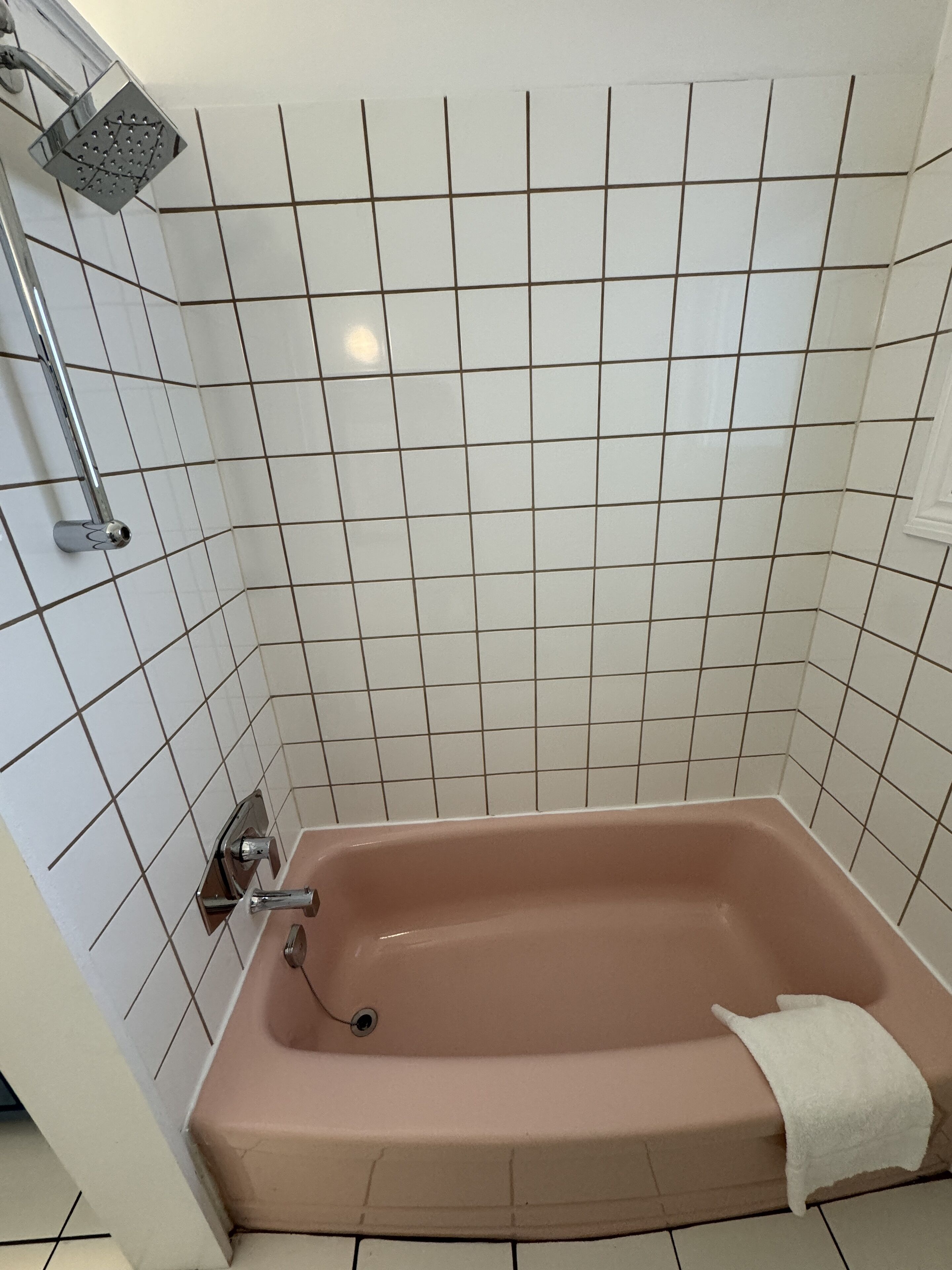 A bathroom with a bathtub, a showerhead, and a towel on the tub.