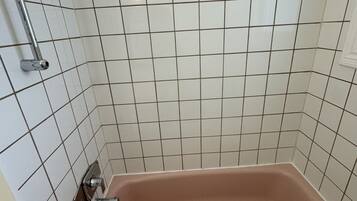 A bathroom with a bathtub, a showerhead, and a towel on the tub.