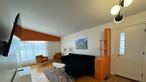 A modern living room with a dark blue sofa, two armchairs, a coffee table, and a TV mounted on the wall. - Hojo House Winnipeg (Winnipeg)