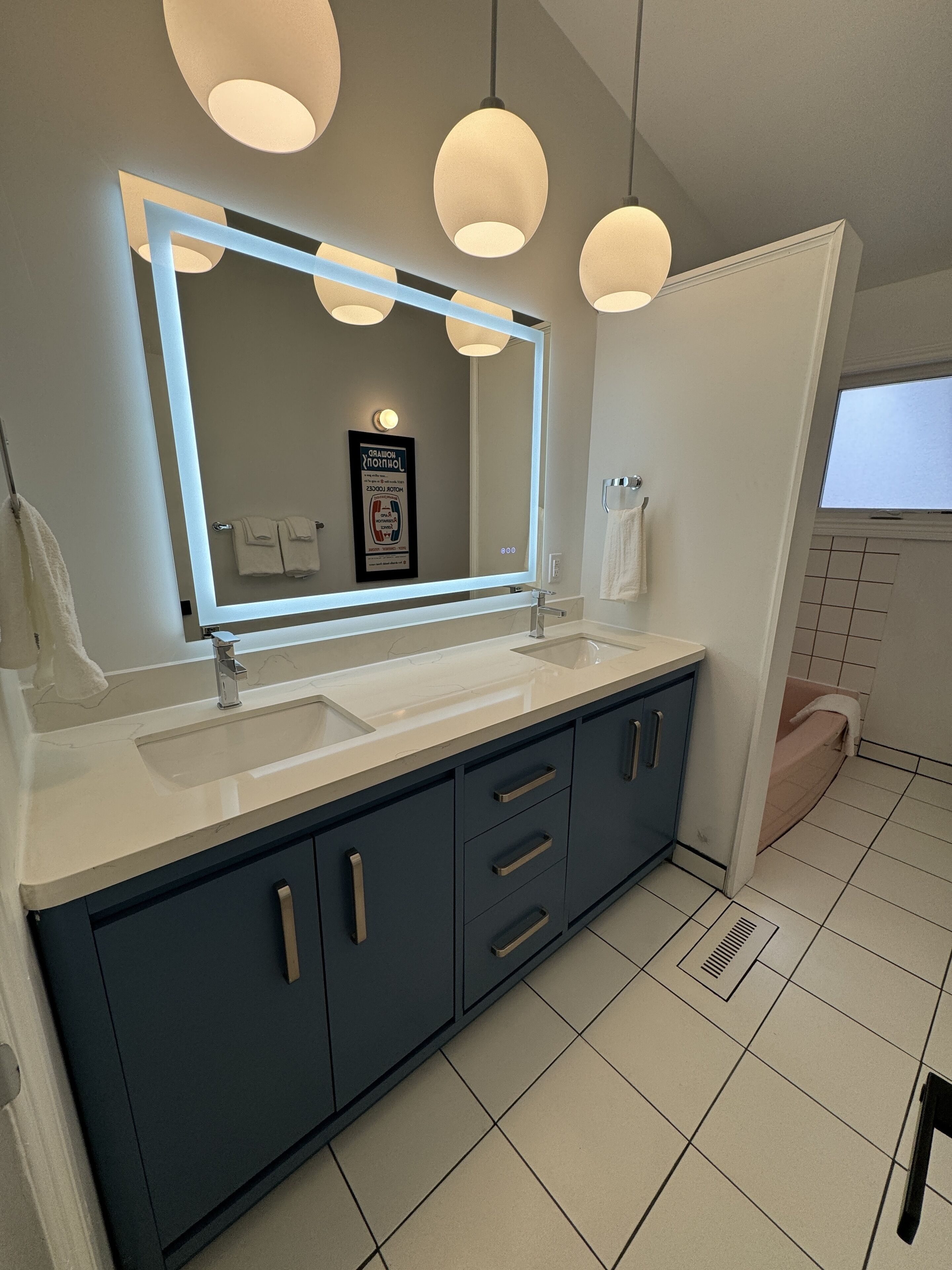 Une salle de bain moderne avec un grand miroir, deux vasques et des meubles de rangement bleu foncé.