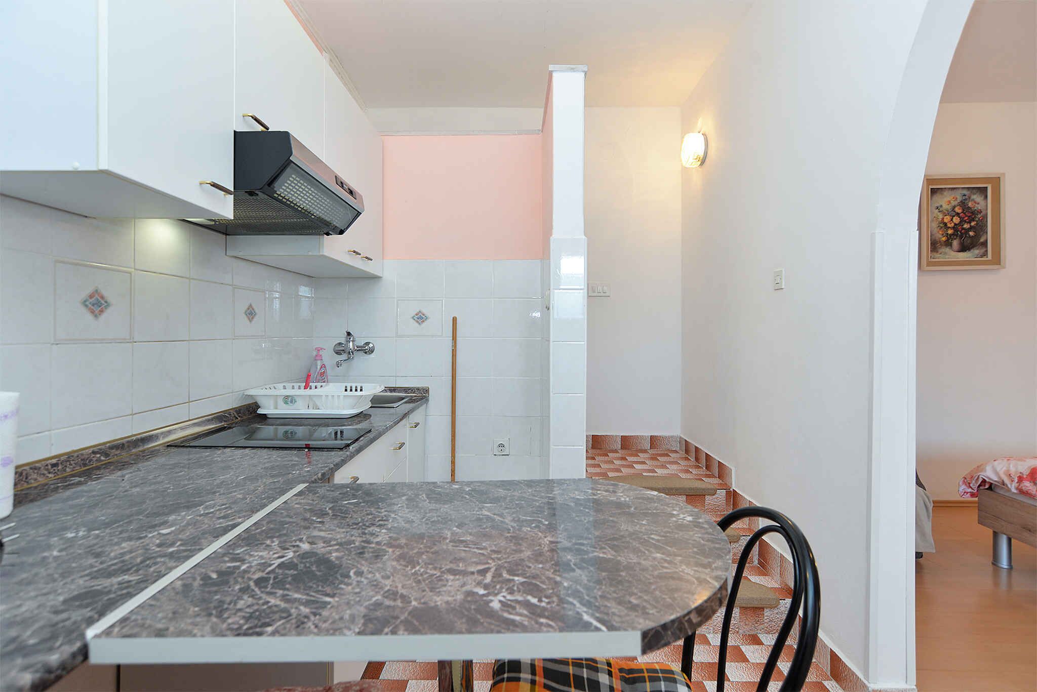 Een keuken met een marmeren aanrecht, witte kasten en een spoelbak.