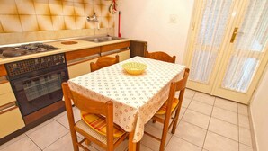 A compact kitchen with a gas stove, oven, and sink. There is a dining table with four chairs, and a window with curtains.