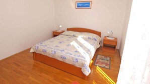 A bedroom with a wooden bed, two bedside tables, a night lamp, a framed picture on the wall, and a patterned rug on the floor.