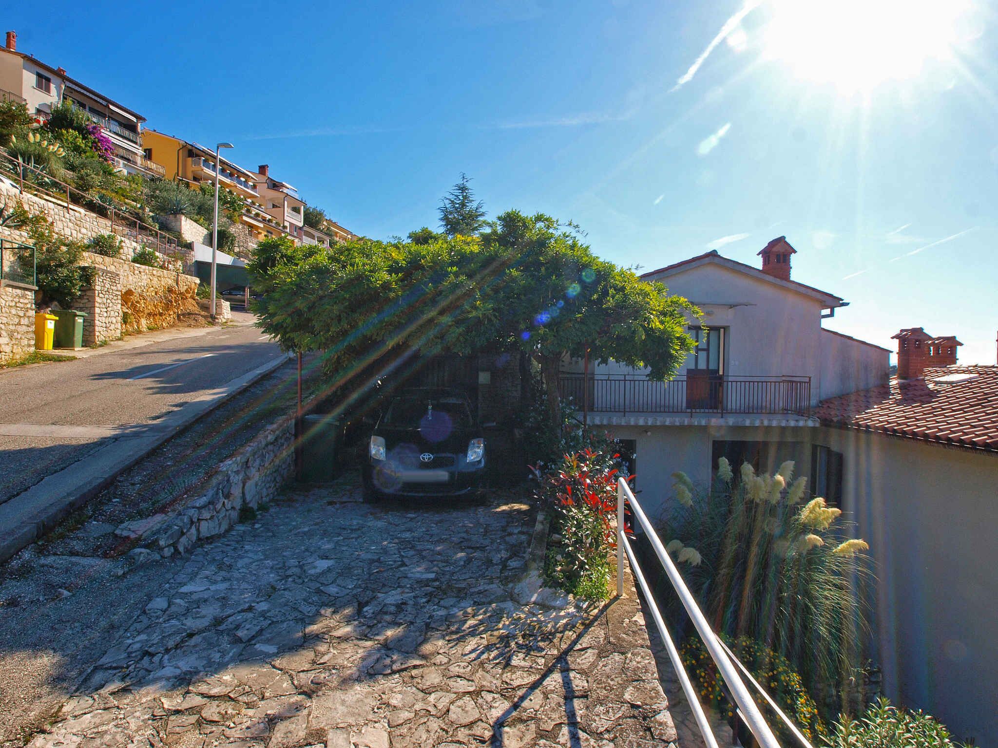 A narrow cobblestone street with a parked car, stone walls, and a building with a balcony.