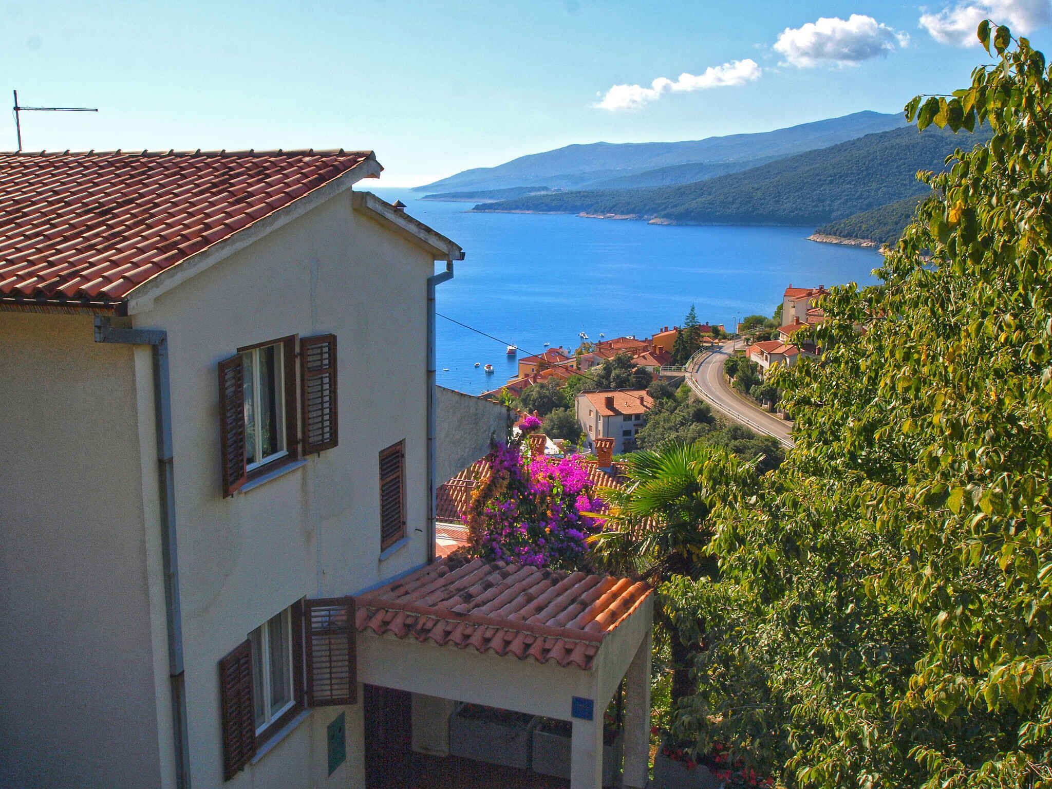 A coastal building with a tiled roof, a view of the sea, and a winding road leading to a town.
