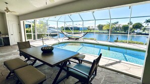 A pool area with a dining table and chairs, a hammock, and a view of a body of water and surrounding landscape. - Punta Gorda Canal Waterfront I Pool, Kayaks, Bikes, Boat Dock (Punta Gorda)