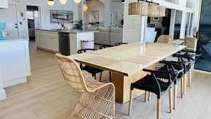 A modern kitchen with a central island, white cabinetry, and a dining area with a large table and wicker chairs. - Punta Gorda Canal Waterfront I Pool, Kayaks, Bikes, Boat Dock (Punta Gorda)