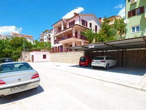 A street with parked cars and a building with balconies and a stone wall.